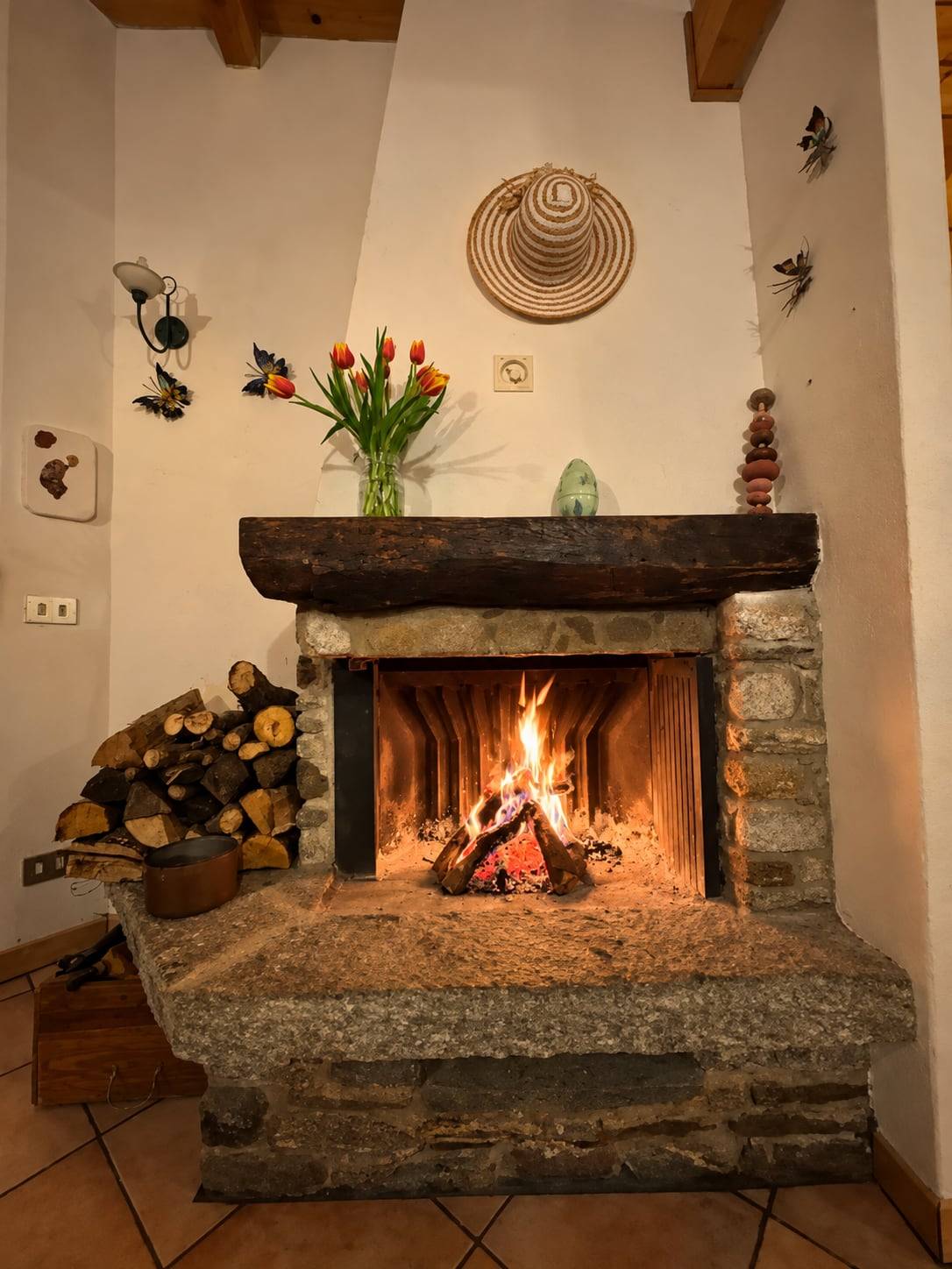 Peisen i Villa Oppilia med hylle i stein, blomster og ved stablet ved siden av